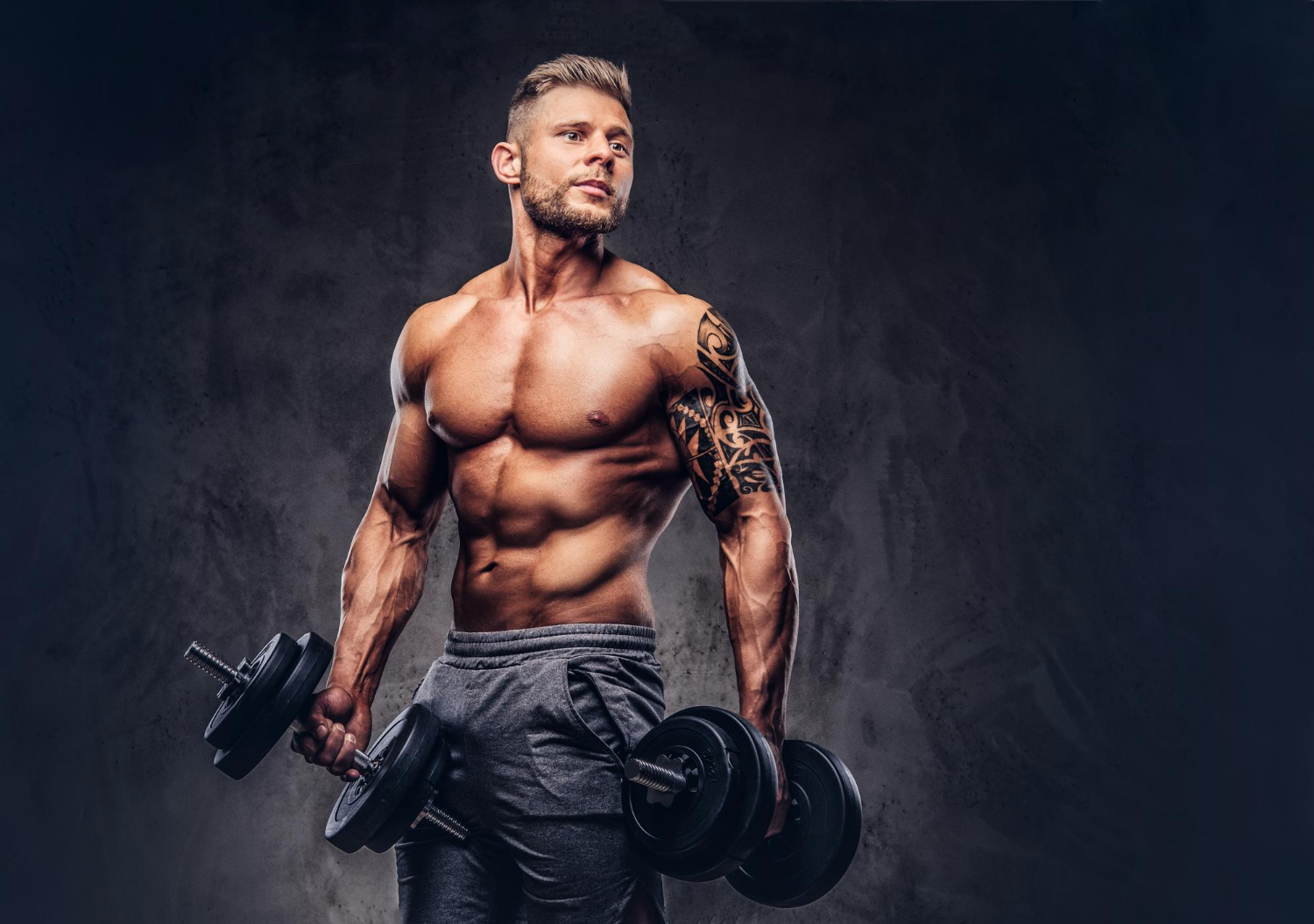 powerful-stylish-bodybuilder-with-tattoo-his-arm-doing-exercises-with-dumbbells-isolated-dark-background