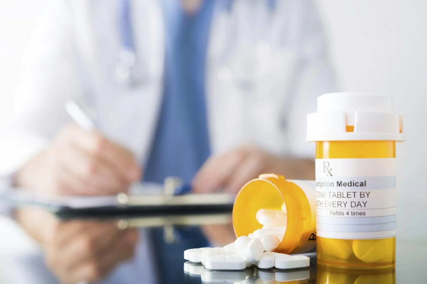 A spilled prescription bottle with tablets, while a doctor writes in the background, symbolizing the prior authorization process for medication and how long it takes.